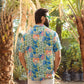 Back view of a man wearing a floral short sleeve casual shirt in a tropical setting