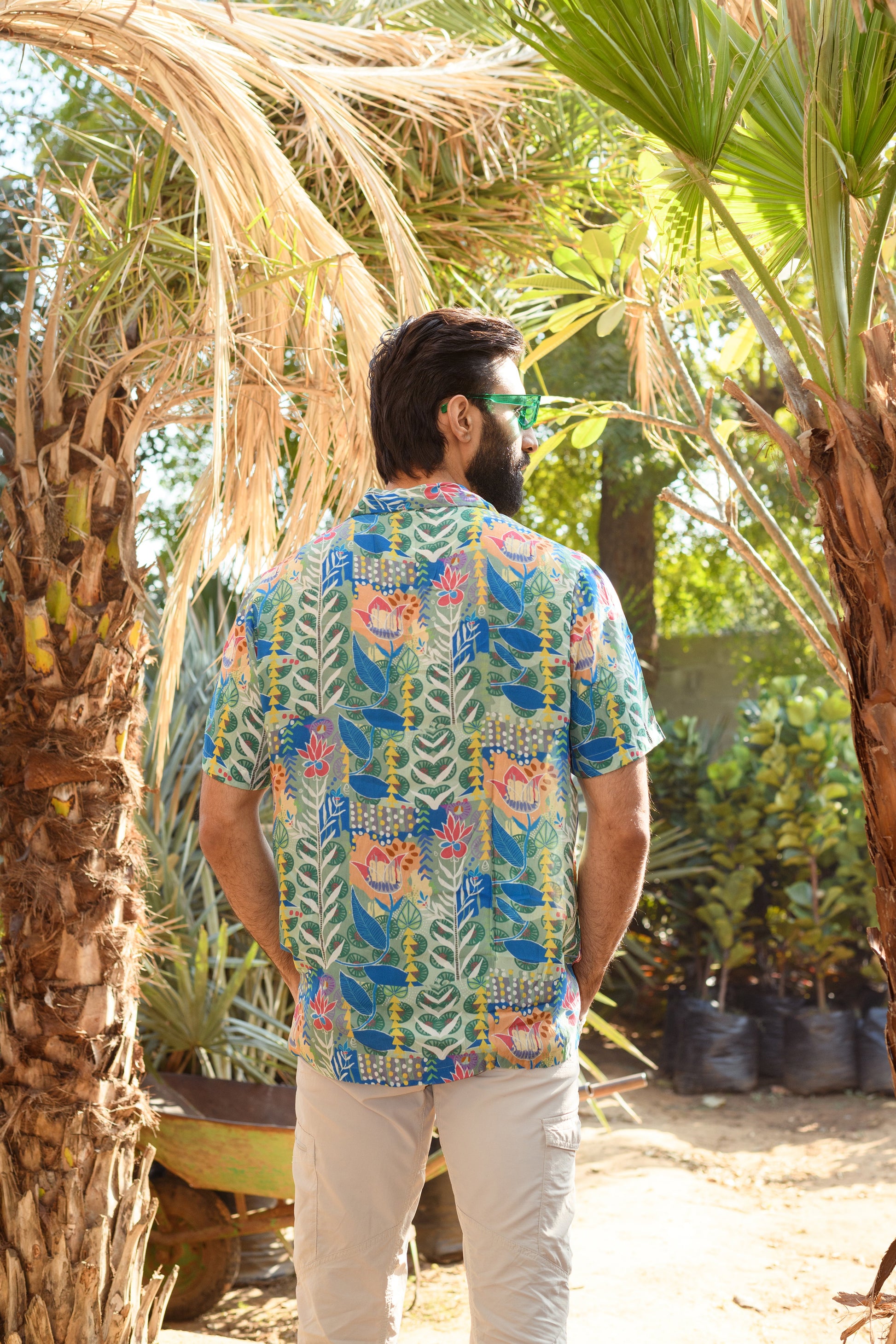 Back view of a man wearing a floral short sleeve casual shirt in a tropical setting