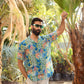 Man wearing a floral short sleeve casual shirt in a tropical outdoor setting surrounded by palm trees