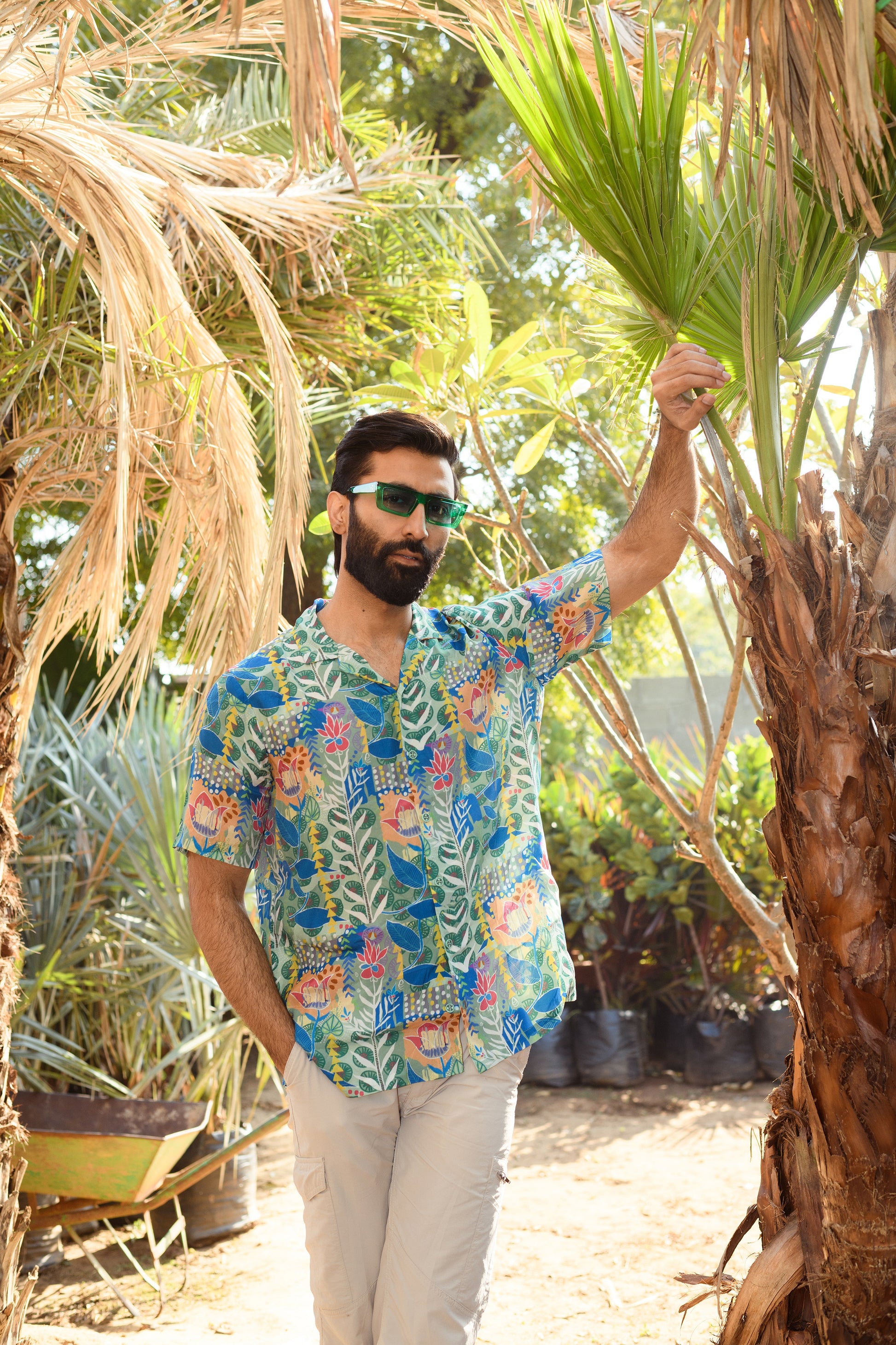 Man wearing a floral short sleeve casual shirt in a tropical outdoor setting surrounded by palm trees