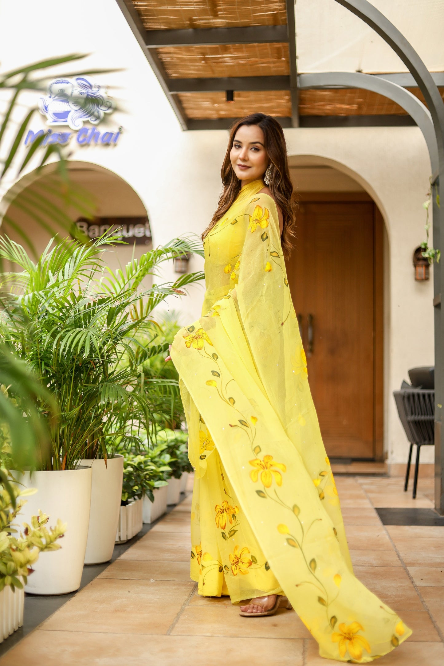 Bright yellow floral viscose chiffon saree with mukaish work, elegantly worn outdoors