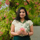 Woman wearing a green embroidered linen top by Stylera holding pink flowers outdoors
