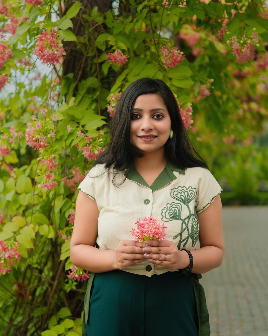 Woman wearing a green embroidered linen top by Stylera holding pink flowers outdoors