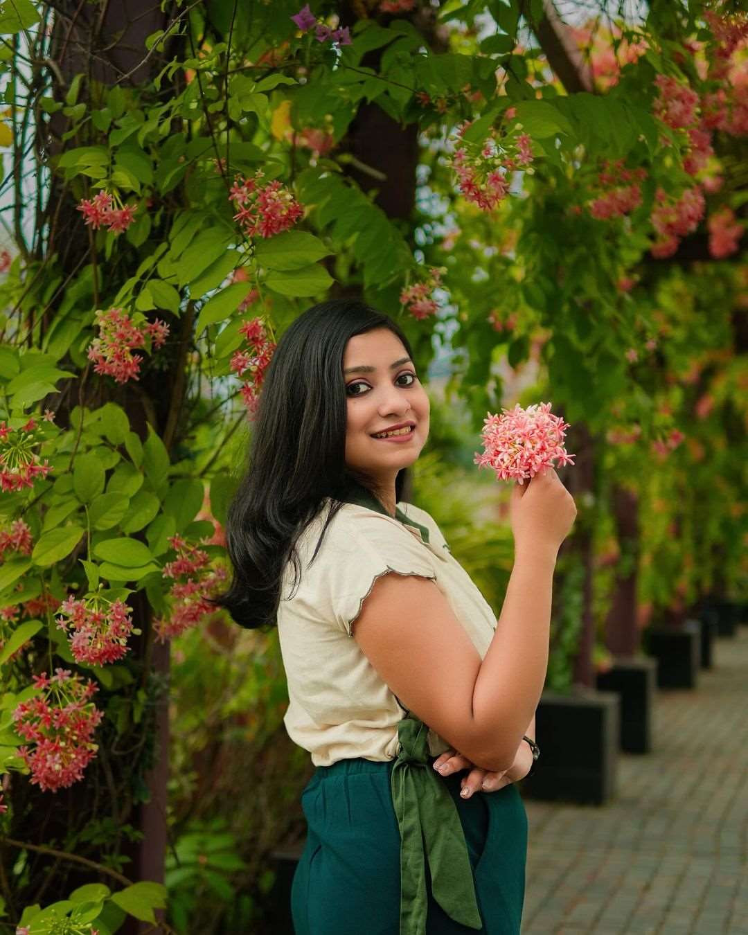 Woman wearing a green embroidered linen top by Stylera standing outdoors near flowering trees