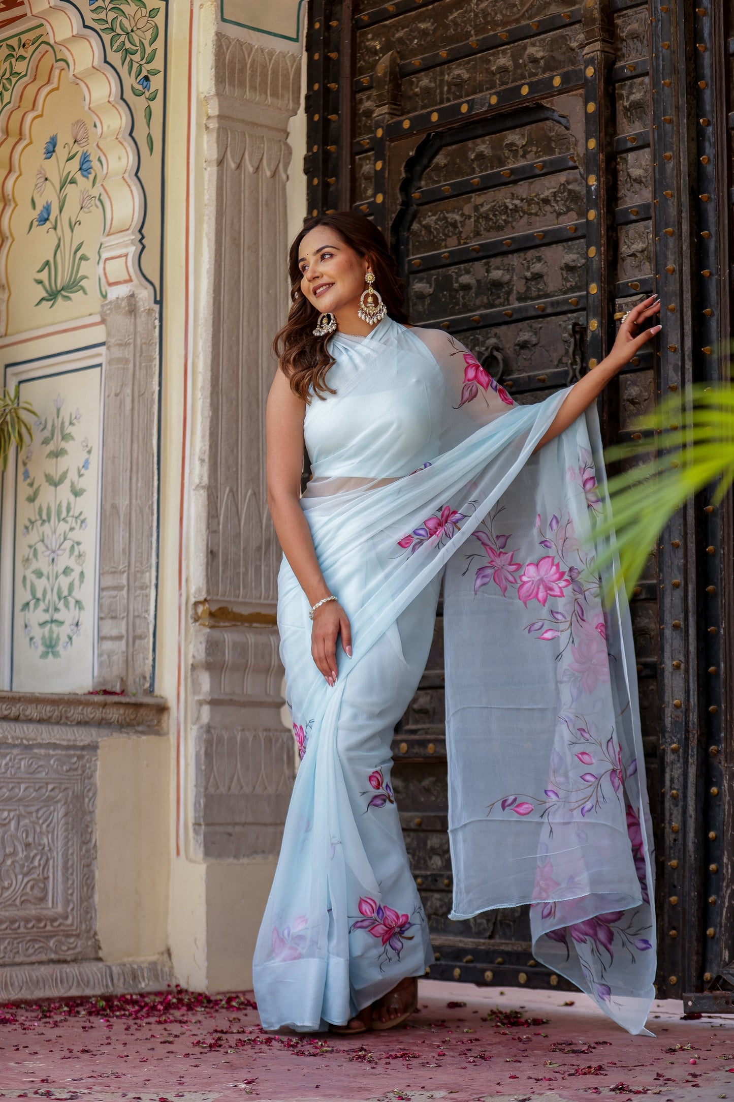 Elegant woman wearing a handcrafted saree with floral print standing near an ornate door