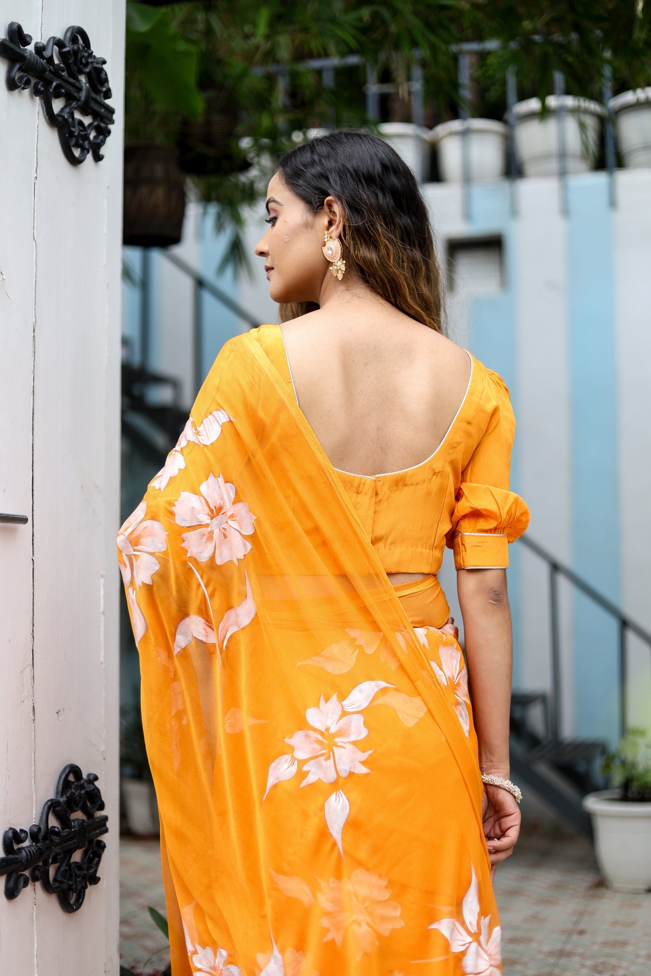 Elegant handpainted chiffon saree in vibrant orange with floral designs, styled for modern occasions