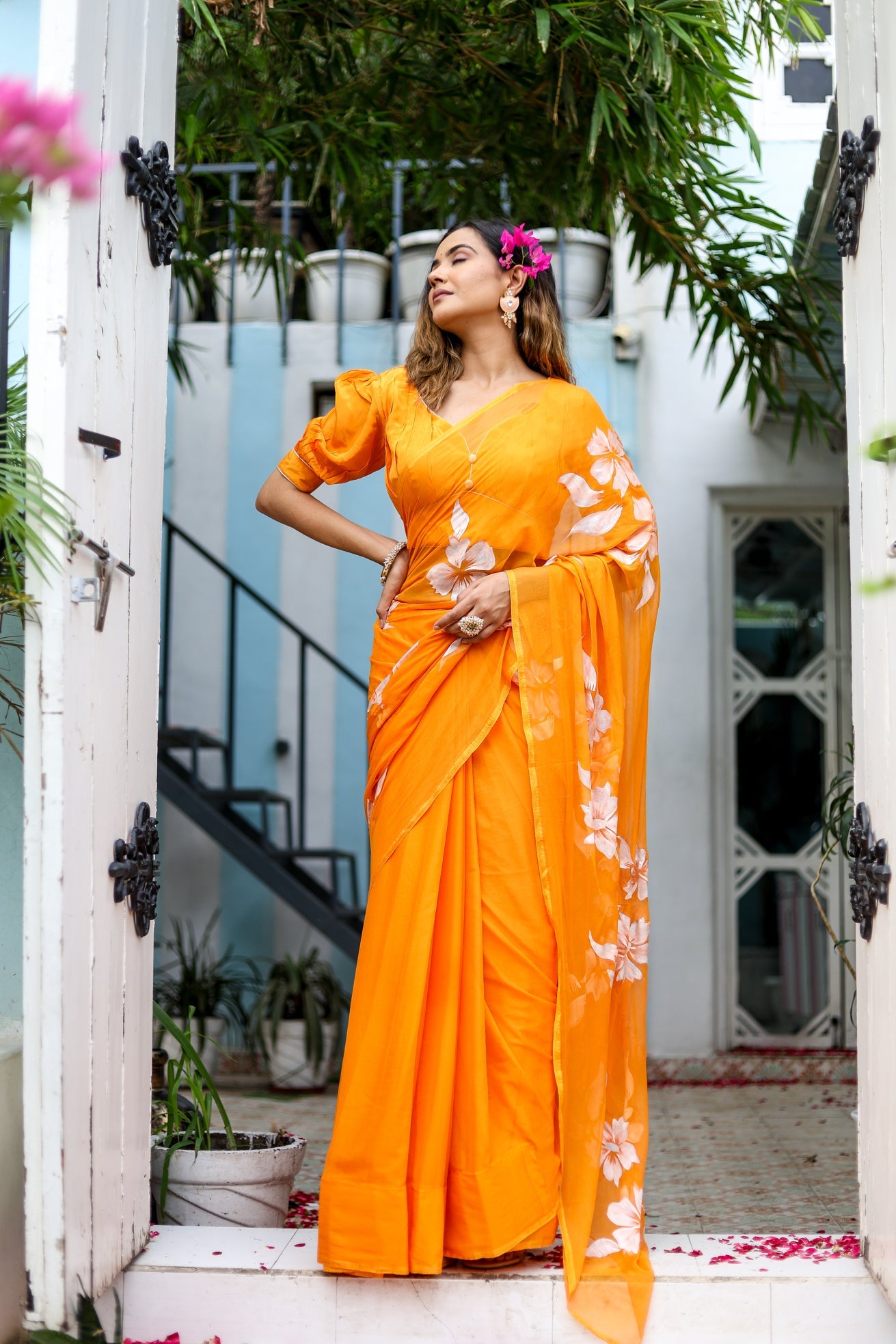 Elegant model in an orange handpainted chiffon saree with floral designs, posing outdoors
