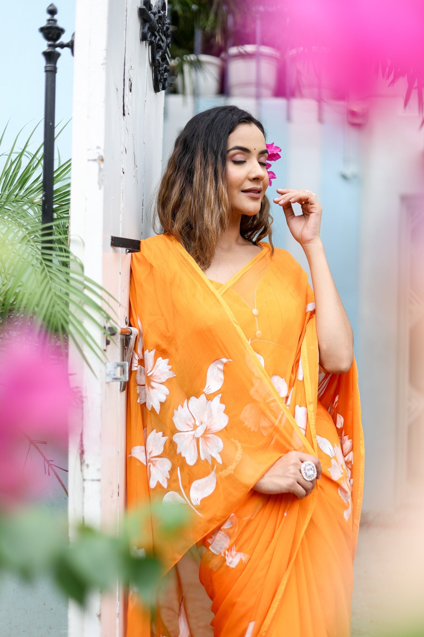 Elegant woman posing in a bright orange handpainted chiffon saree adorned with floral designs