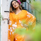 Elegant woman wearing a handpainted chiffon saree in vibrant orange with floral designs, posing outdoors