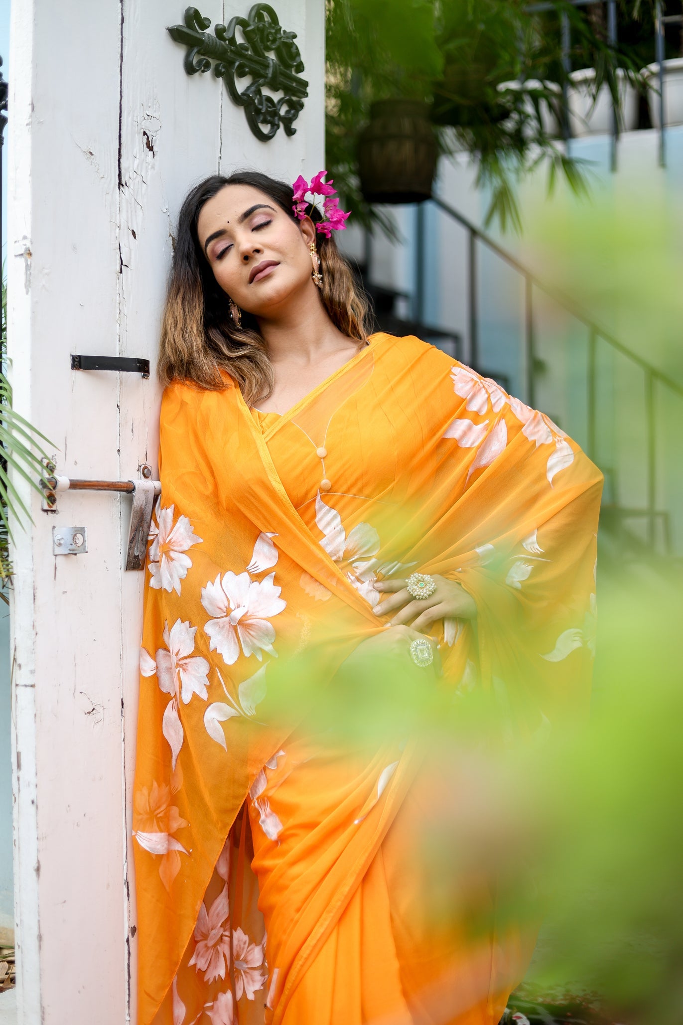 Elegant woman wearing a handpainted chiffon saree in vibrant orange with floral designs, posing outdoors