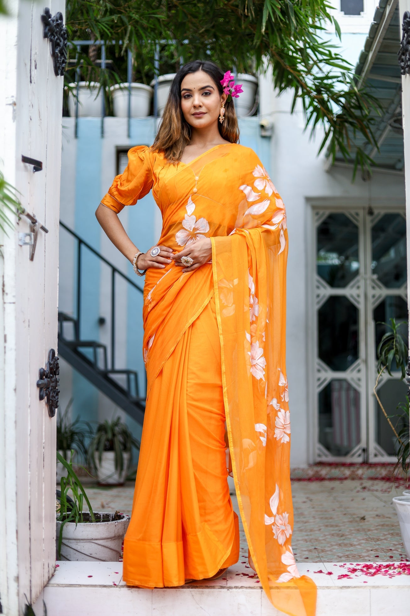 Elegant handpainted chiffon saree in vibrant orange with botanical designs, perfect for festive occasions