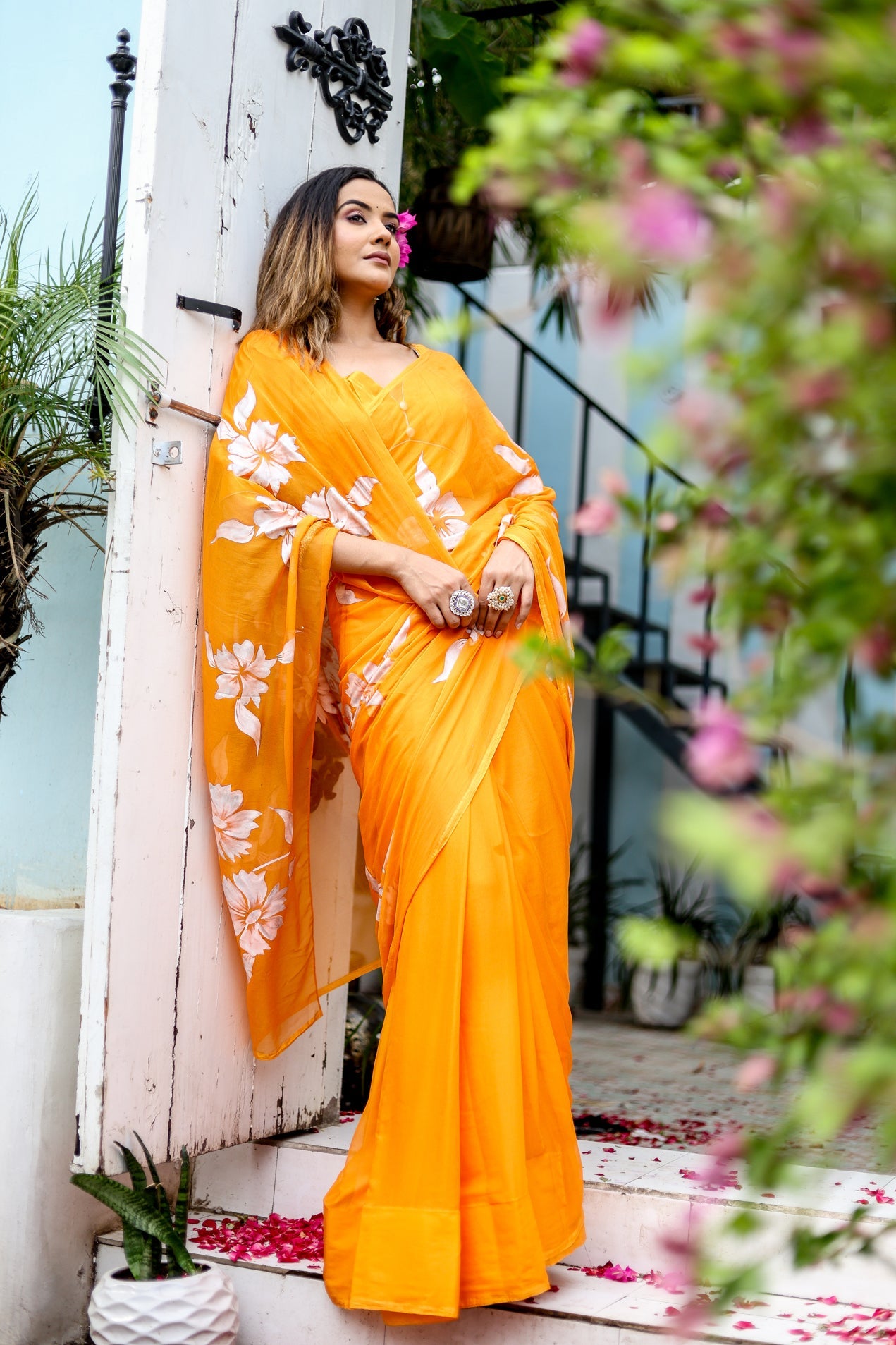 Stylera Handpainted chiffon saree in bright orange with floral patterns, elegantly draped on model
