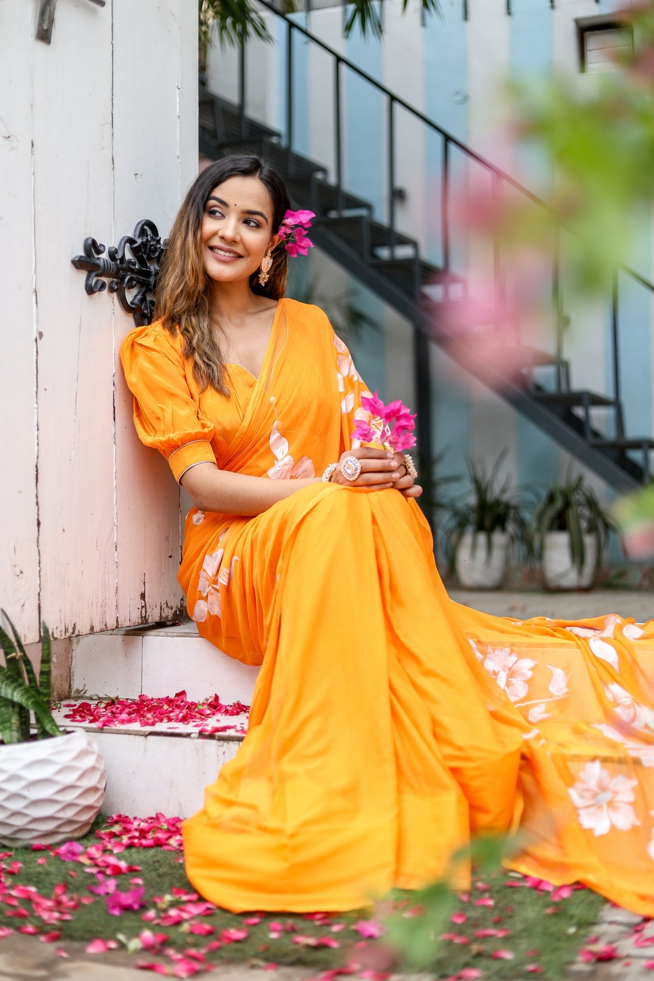 Bright orange handpainted chiffon saree with floral designs, styled elegantly for a special occasion