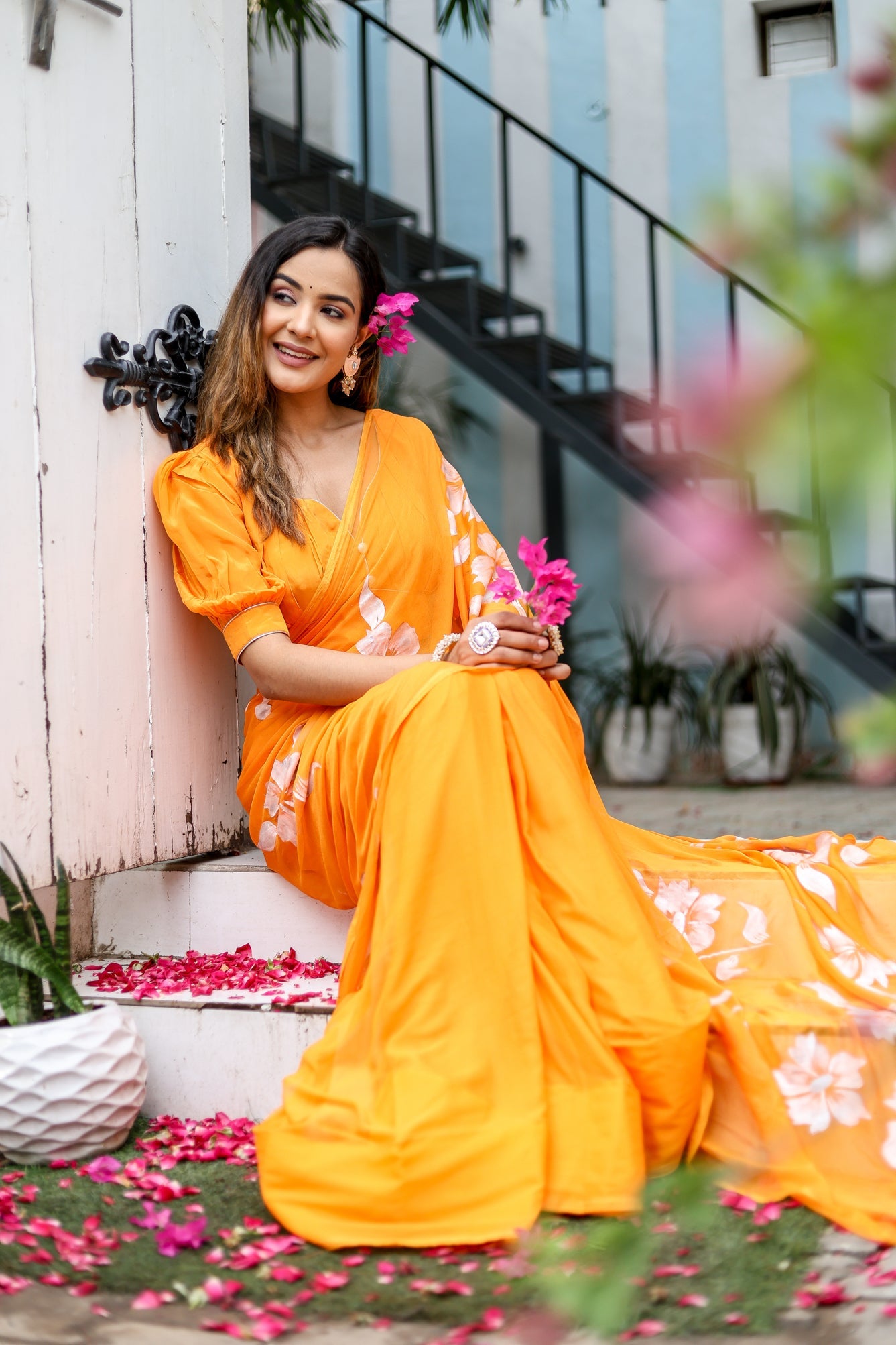 Elegant model wearing a handpainted chiffon saree in orange with floral details, posing gracefully outdoors