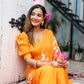 Beautiful woman wearing a handpainted chiffon saree in vibrant orange, adorned with floral accents