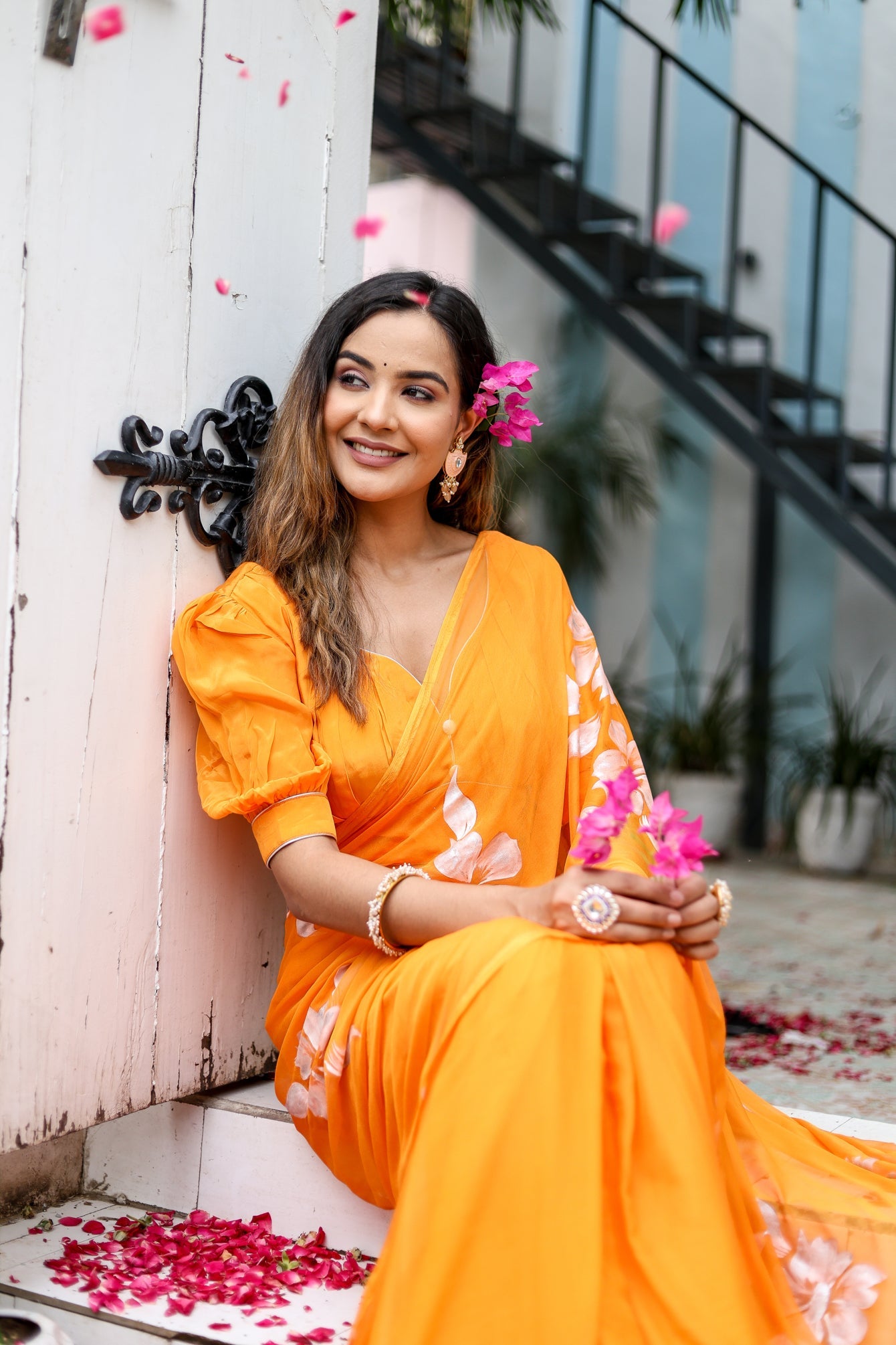 Beautiful woman wearing a handpainted chiffon saree in vibrant orange, adorned with floral accents