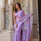 Elegant woman in a handpainted lavender chiffon saree with floral patterns, set against a decorative backdrop