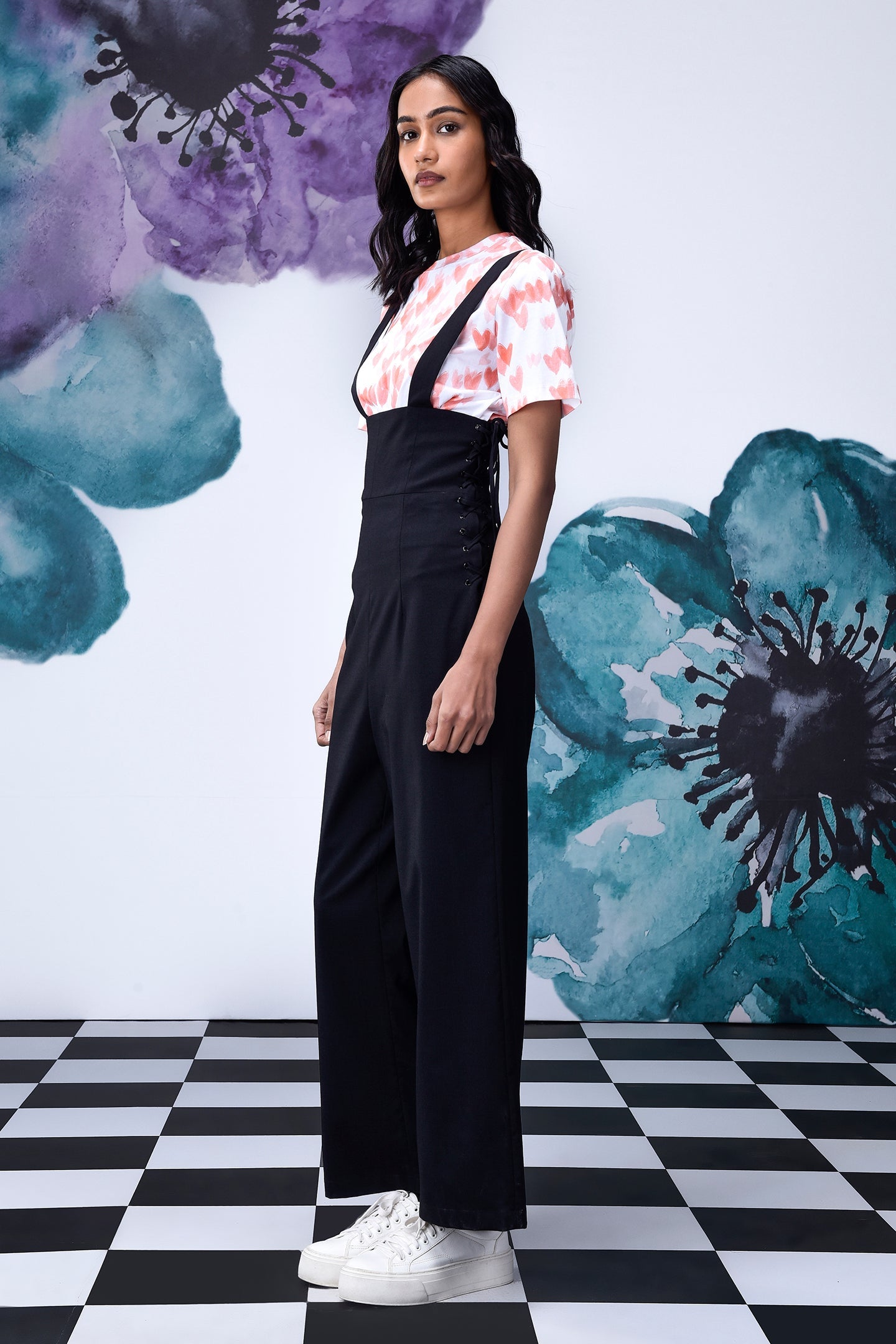 Stylera model wearing black high waist lace up overalls with wide legs and white sneakers