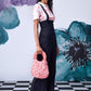 Stylera model wearing black dungaree styled high waist lace up overalls with pink floral handbag and white sneakers