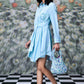 Model wearing Stylera blue green stripe dress with waist tie carrying floral handbag on checkerboard floor