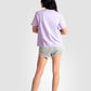 Back view of woman wearing lavender graphic t-shirt for women paired with denim shorts and sneakers