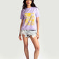 Woman wearing lavender graphic t-shirt for women with yellow design paired with denim shorts and sneakers