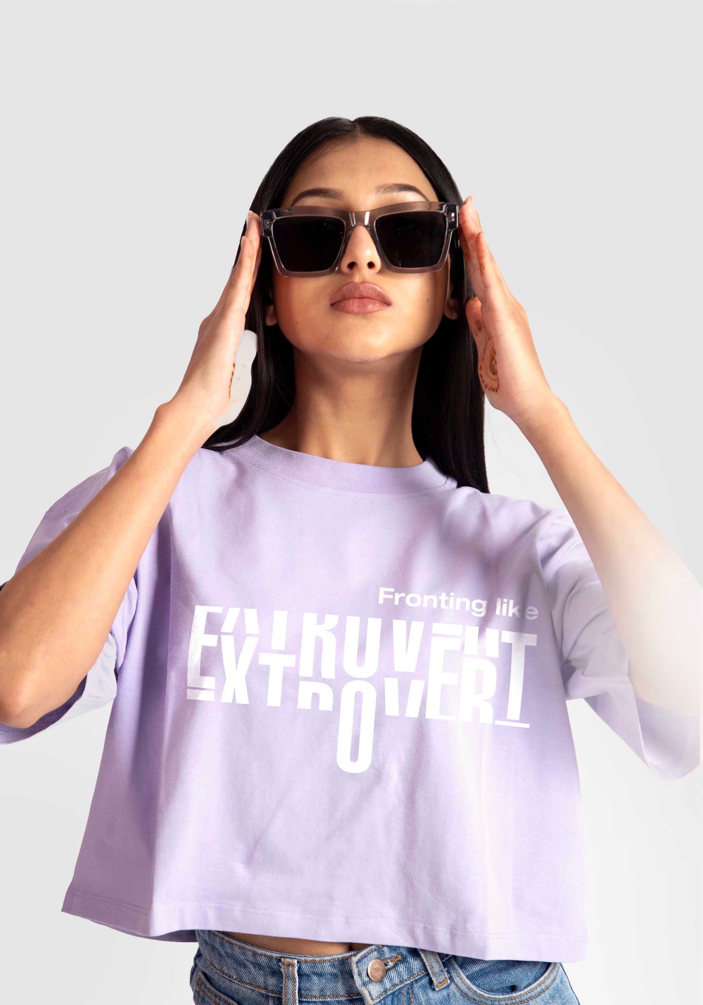 Stylera lavender oversized crop top with white text worn by woman adjusting sunglasses