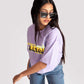 Woman wearing lavender oversized crop top with graphic print paired with blue jeans and sunglasses