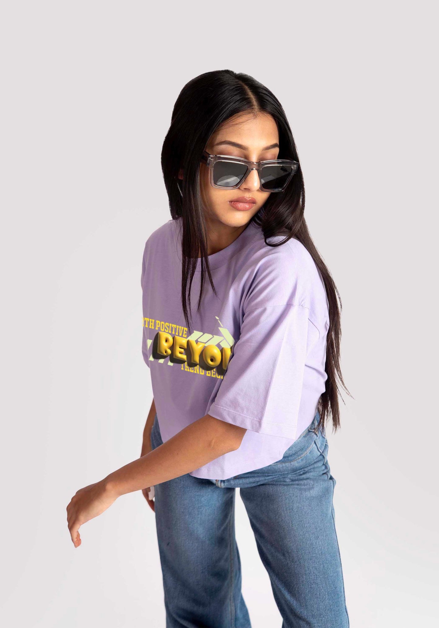 Woman wearing lavender oversized crop top with graphic print paired with blue jeans and sunglasses