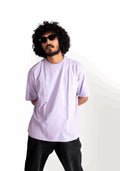 Man wearing a lavender oversized t-shirt by Stylera paired with black pants and sunglasses