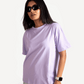 Woman wearing lavender oversized t-shirt with short sleeves paired with ripped jeans and black sunglasses