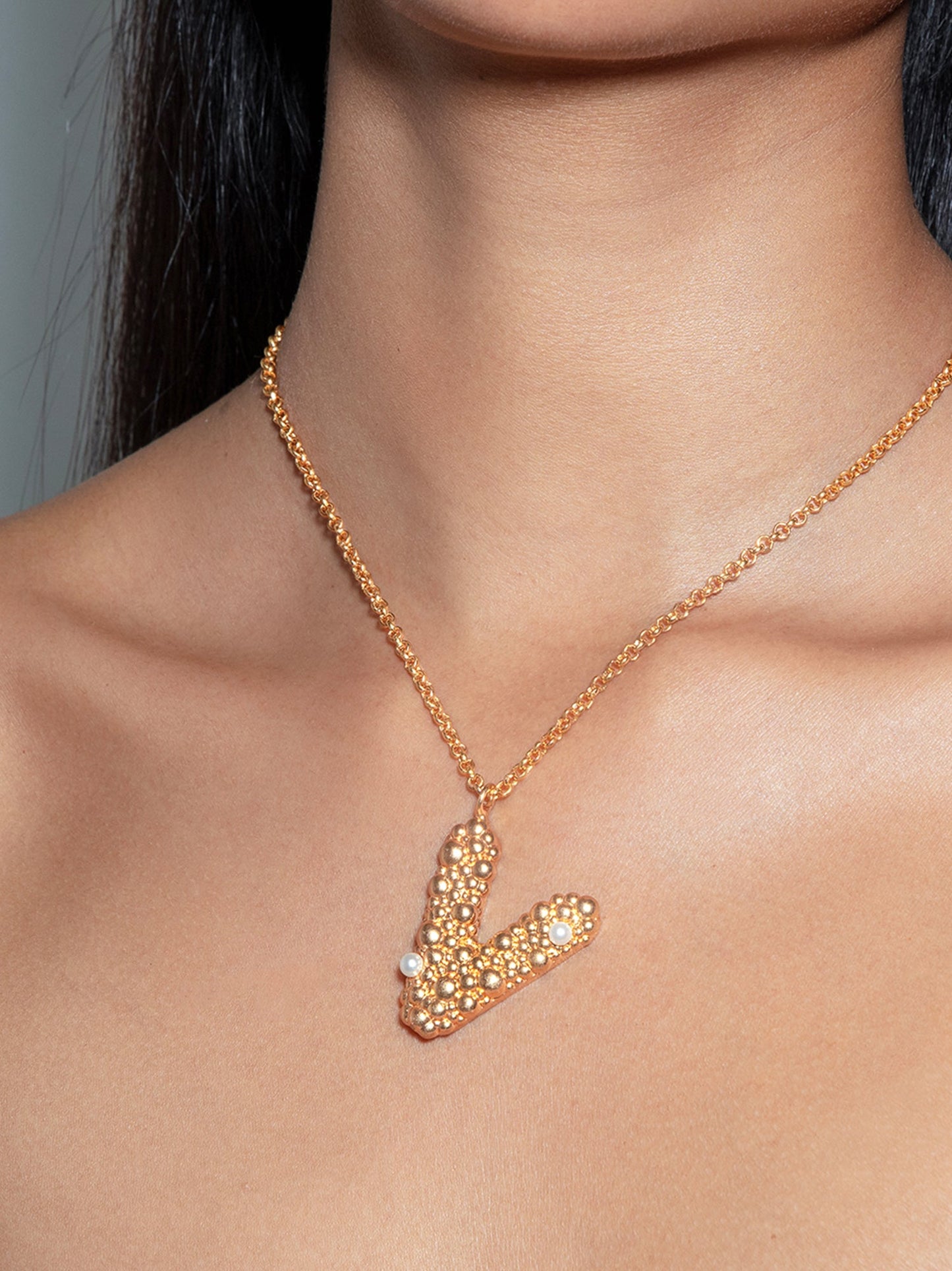 Stylera letter V pendant necklace in gold with crystal and pearl accents on model neckline