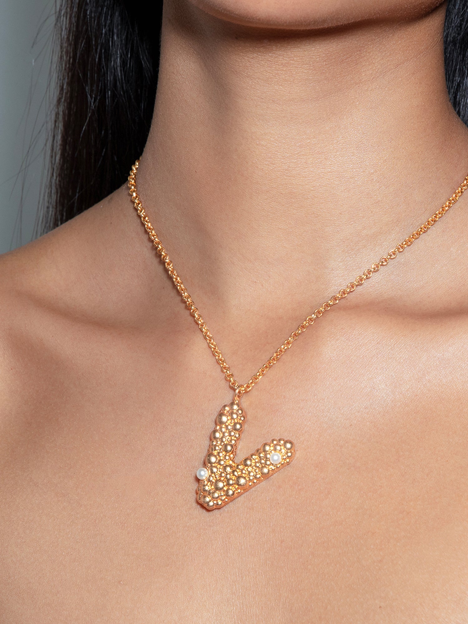 Stylera letter V pendant necklace in gold with crystal and pearl accents on model neckline