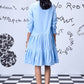 Back view of model wearing light blue sequin dress by Stylera with tiered skirt and white sneakers