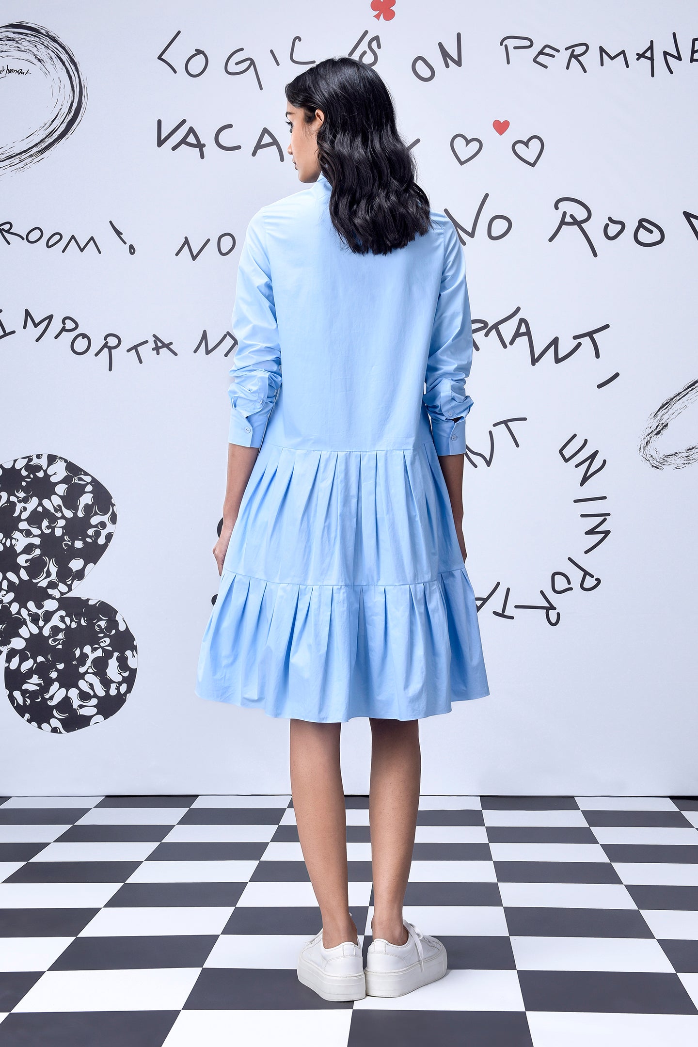 Back view of model wearing light blue sequin dress by Stylera with tiered skirt and white sneakers