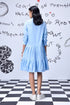 Back view of model wearing light blue sequin dress by Stylera with tiered skirt and white sneakers