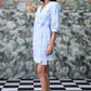 Stylera model wearing a knee length light blue wrap dress with three quarter sleeves and tie waist