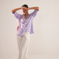 Woman wearing Stylera light purple fashion top with ruffle details and white pants