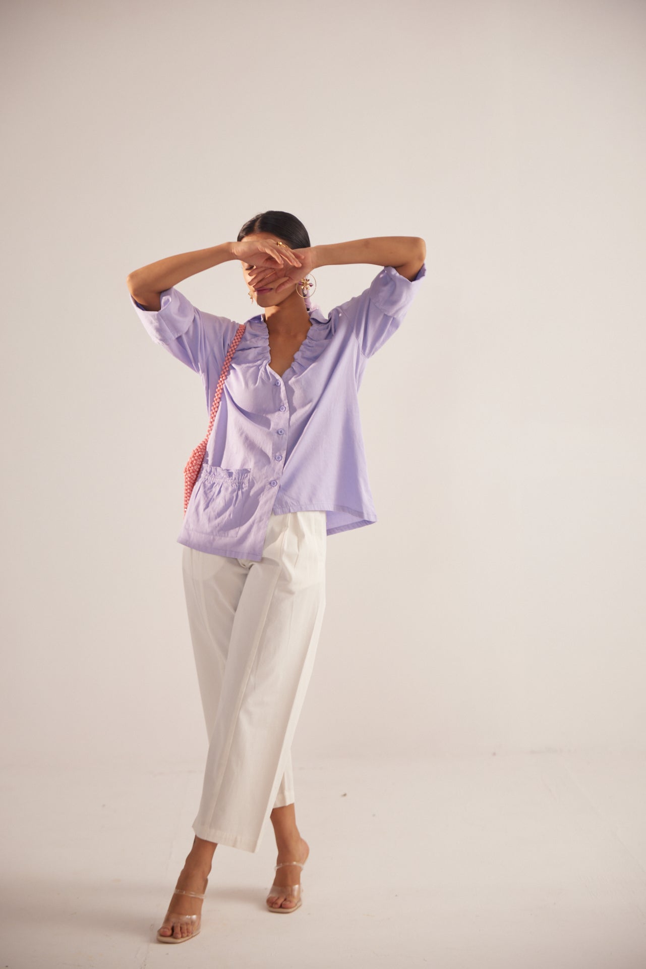 Woman wearing Stylera light purple fashion top with ruffle details and white pants