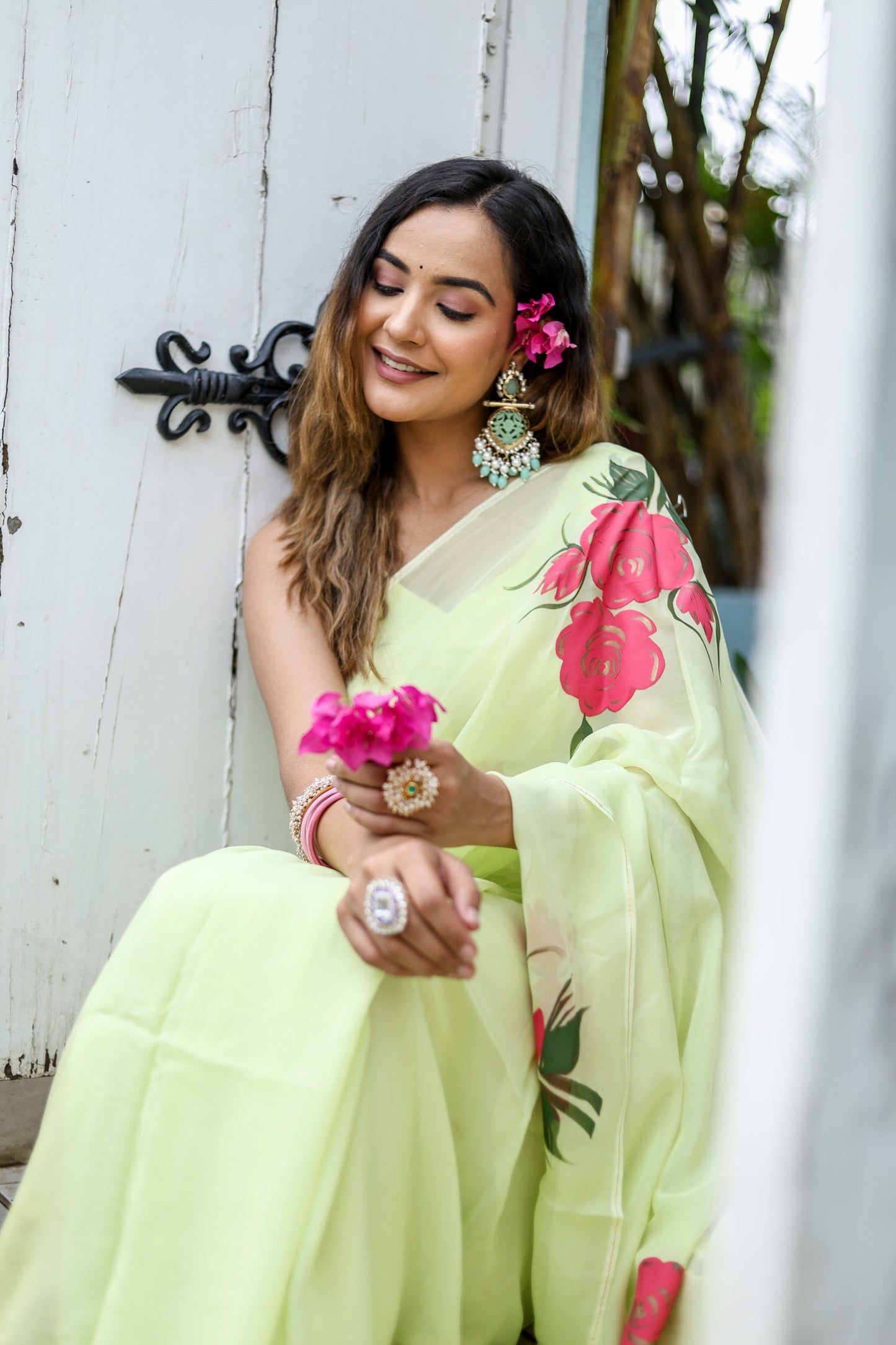 Model wearing a lightweight pastel saree with floral print, sitting gracefully and holding flowers