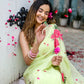 Model wearing a lightweight pastel saree with floral print, surrounded by flower petals in a vibrant setting