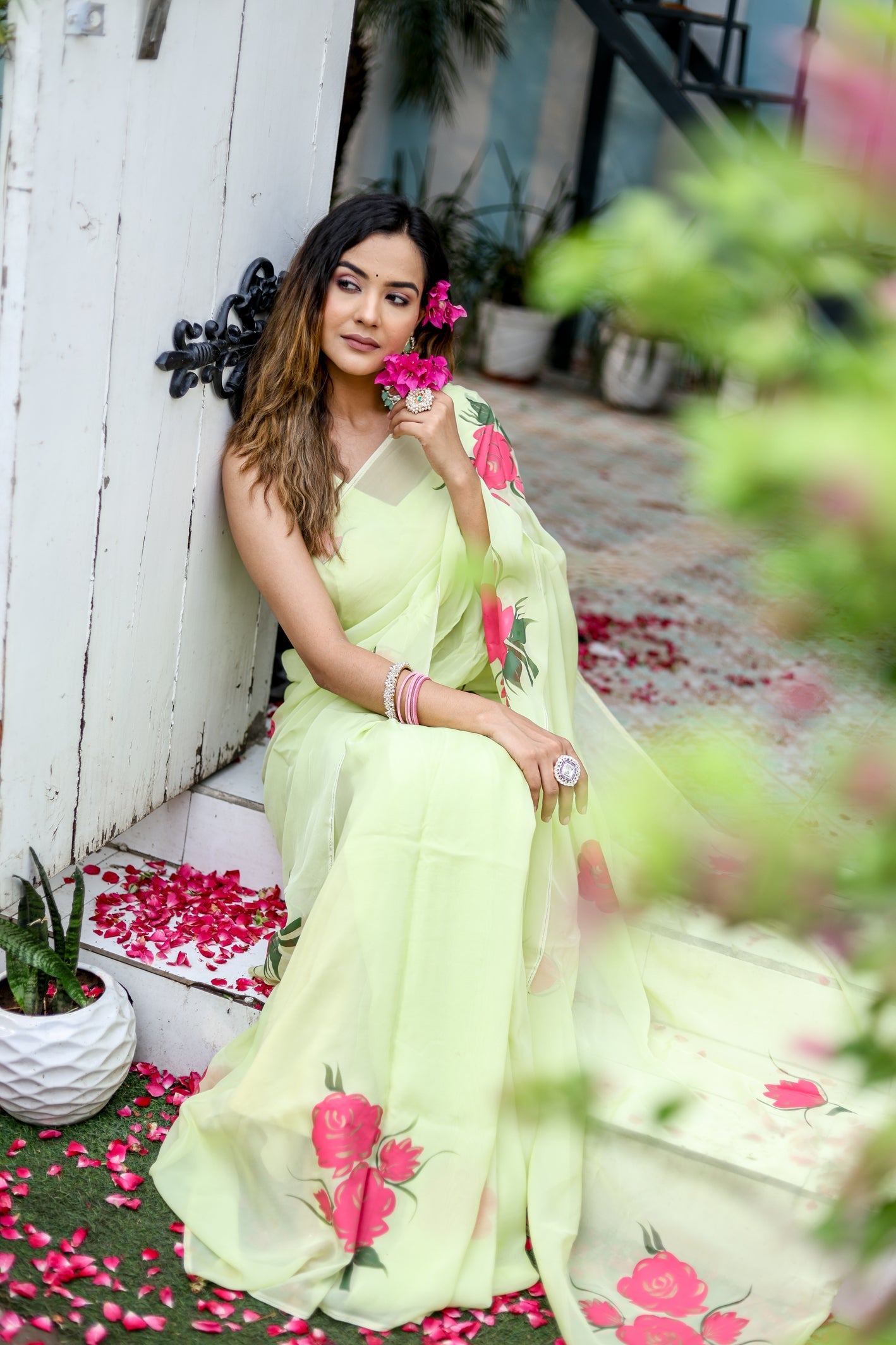 Model wearing a lightweight pastel saree with floral print, sitting among flowers and greenery