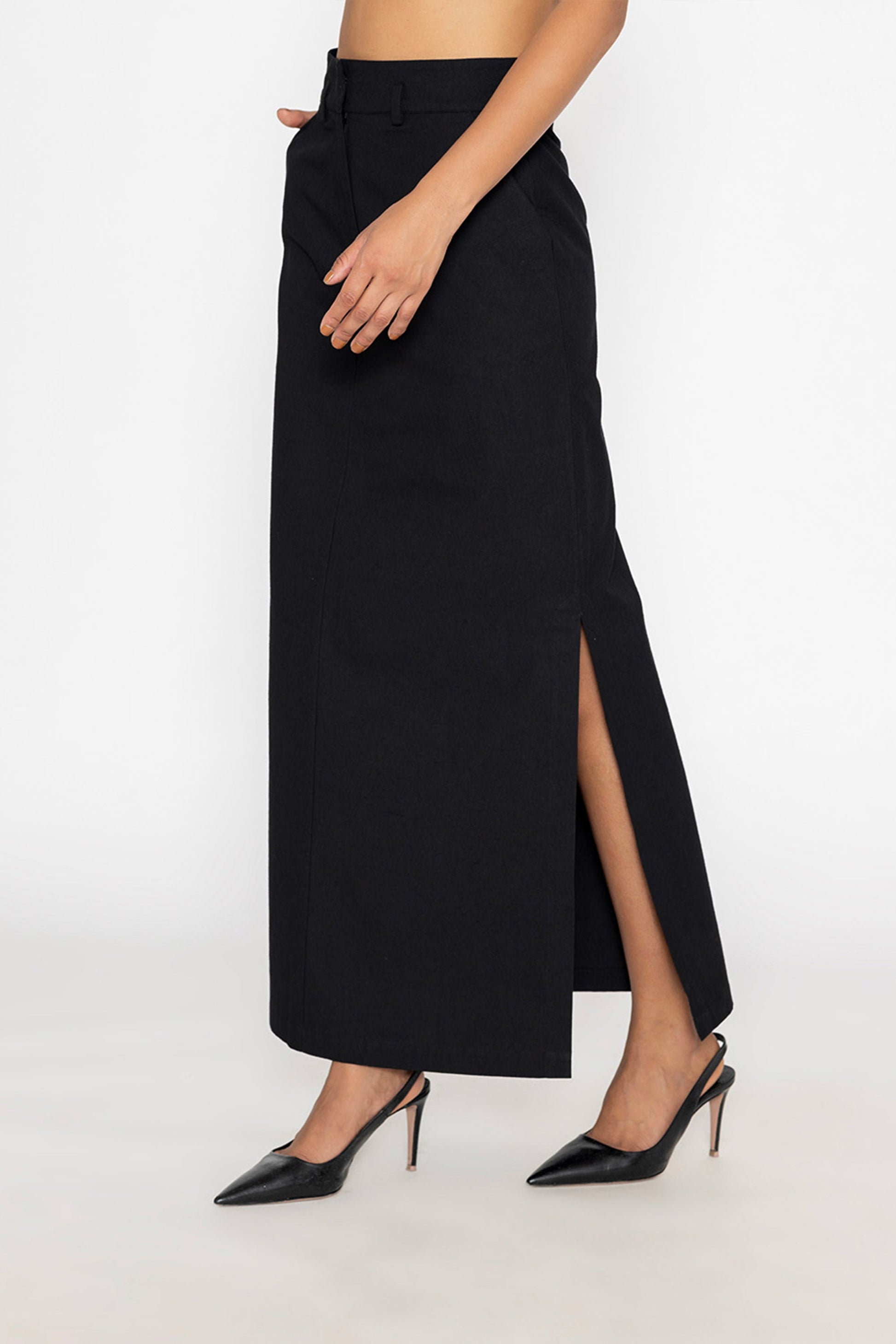Woman wearing a long black skirt with slit from Stylera paired with black pointed heels