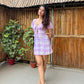 Model wearing Stylera trendy short sleeve mini dress in lilac plaid with tie front and sandals on bamboo patio