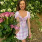 Young woman smiling in Stylera trendy short sleeve mini dress pink plaid tie front puff sleeves holding roses outdoors