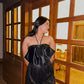 Model wearing Luna Top for women black satin halter top paired with sequin shorts standing by wooden glass pane door