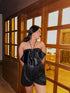 Model wearing Luna Top for women black satin halter top paired with sequin shorts standing by wooden glass pane door
