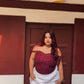 Model wearing red lace corset top for women with white skirt standing against a brown door backdrop