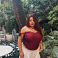 Plus size model wearing a red lace corset top for women with off shoulder tie straps and white skirt in a garden patio