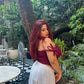 Model wearing Stylera red lace corset top for women with off shoulder bow ties and white skirt in garden patio